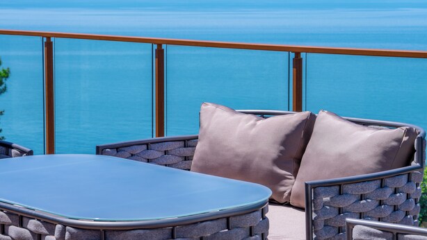 A balcony with a glass table and wicker chairs, overlooking a calm sea. - GREENWOOD (Batumi)