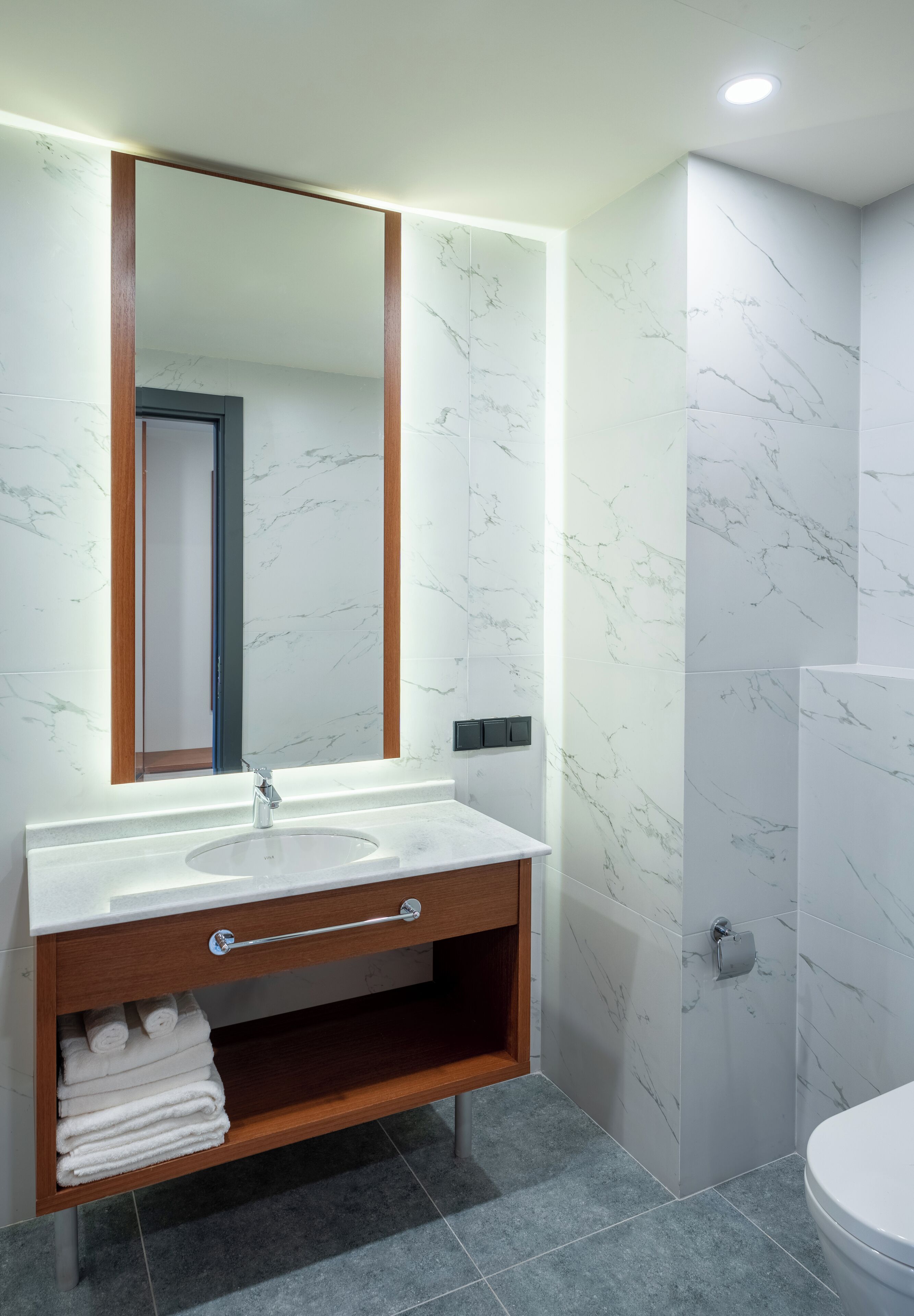 A modern bathroom with a marble vanity, a large mirror, and a toilet.