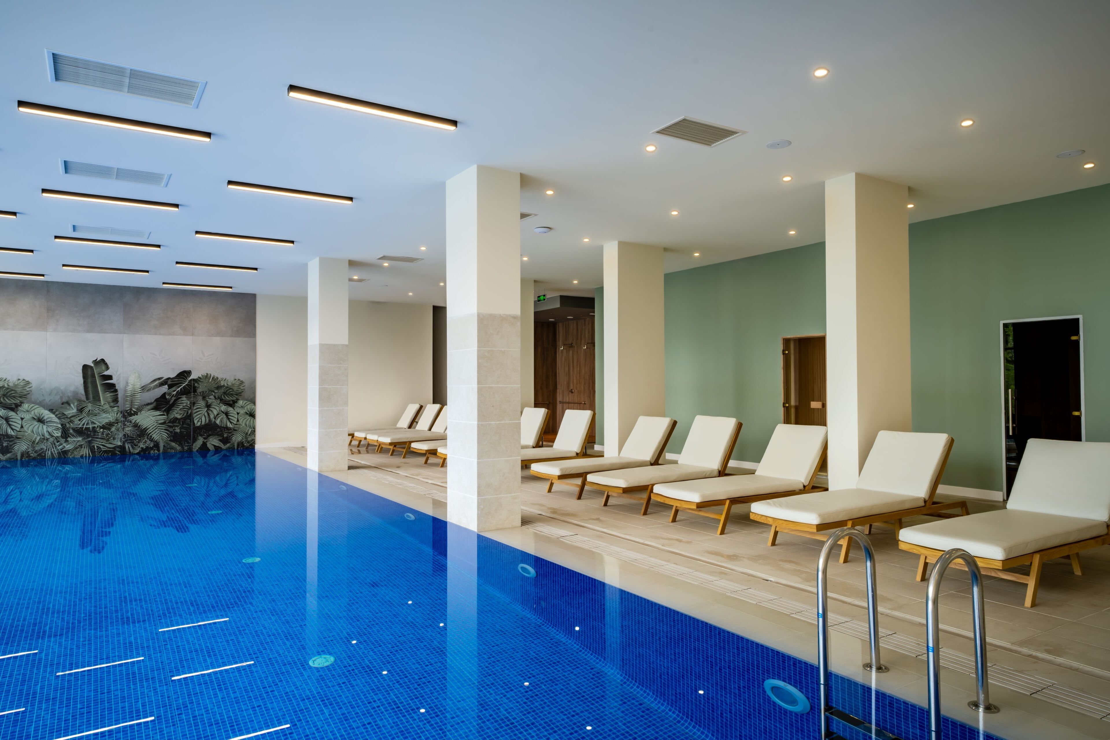 A swimming pool with lounge chairs and a ceiling with recessed lighting.