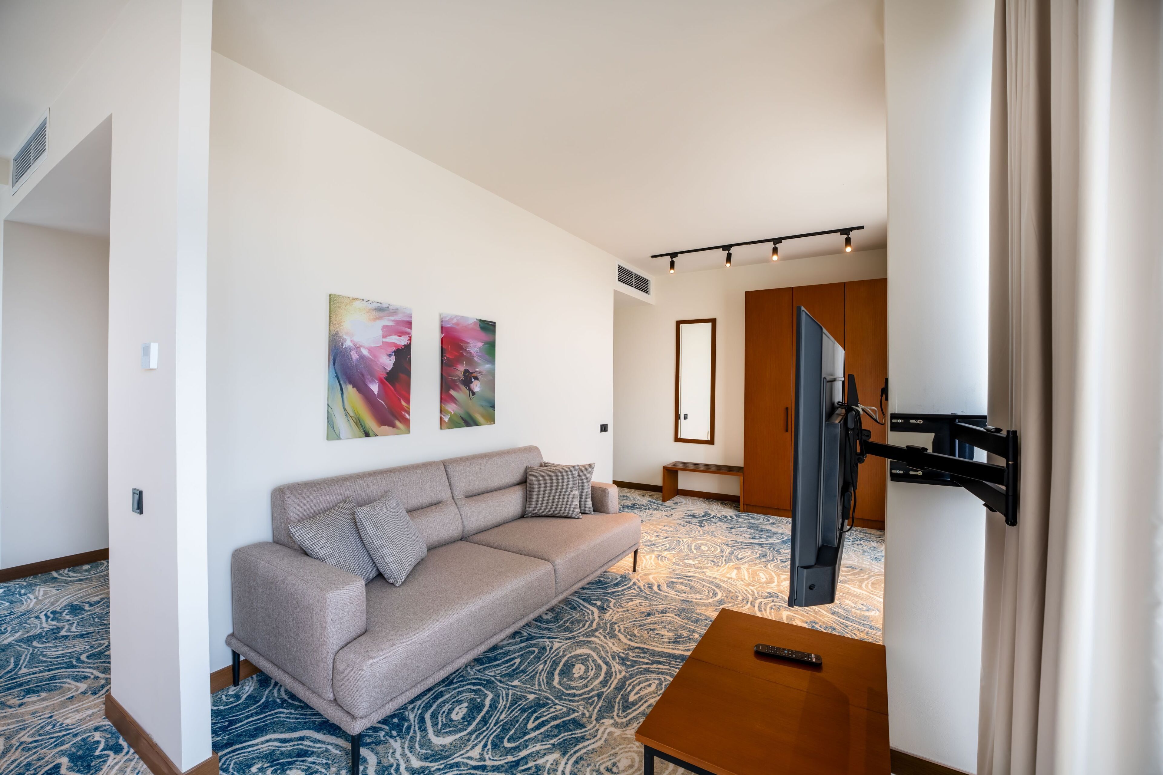 Una sala de estar moderna con un sofá, un televisor montado y arte abstracto en la pared.