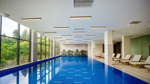 An indoor swimming pool with clear blue tiles, sunlit ceiling lights, and lounge chairs along the side. - GREENWOOD (Batumi)