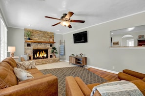 Una sala de estar con chimenea de piedra, sofás de cuero, ventilador de techo y televisor montado.