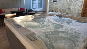 A hot tub with water jets, a stone wall, a blue door, and a wicker sofa. - Bell Haus - Hot Tub, Fire Pit & Walk to Main St (Fredericksburg)