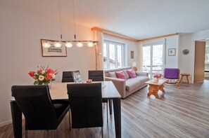 Una sala de estar moderna con comedor, ventanas amplias y piso de madera.