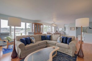 A living room with a sectional sofa, a glass coffee table, and a dining area in the background.