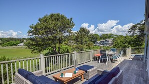 A deck with outdoor furniture, a view of a green field, and a house in the background. - Stunning Marsh Views, Near Pleasant Street Beach! (Chatham)