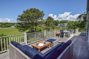 A deck with outdoor furniture, a view of a green field, and a house in the background.
