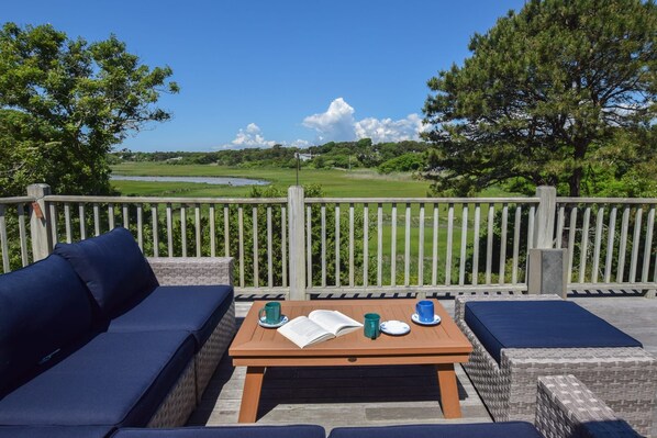 An outdoor seating area with a wooden table, two blue cushioned sofas, and a view of a golf course.