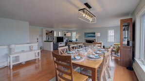 A spacious living area with a dining table set for a meal, a television, and a fireplace. - Stunning Marsh Views, Near Pleasant Street Beach! (Chatham)