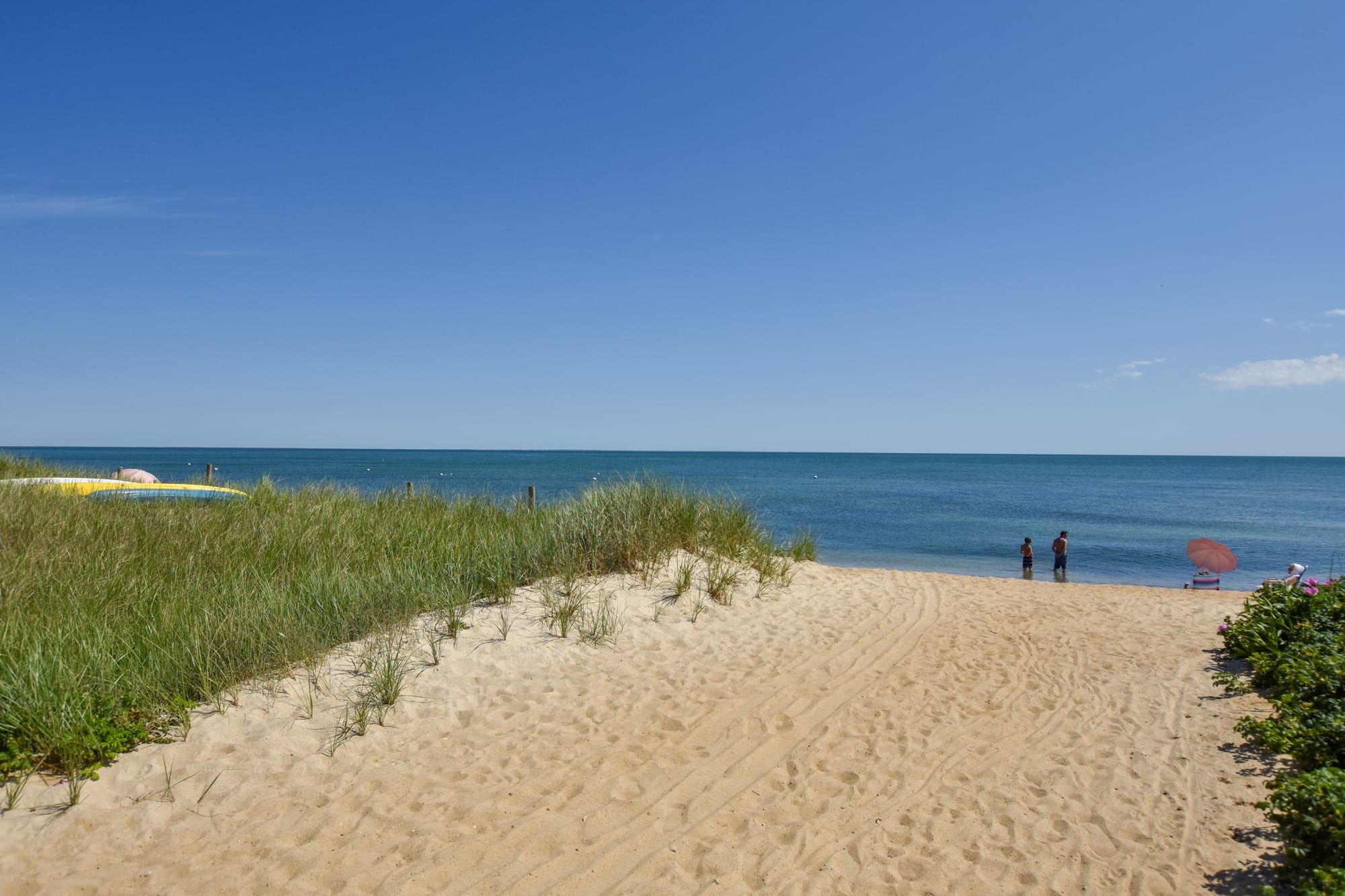 A beach with sand dunes, a clear blue sky, and a calm sea.