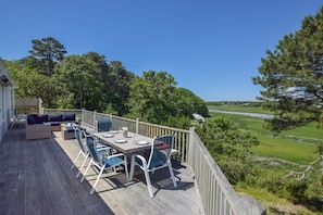A deck with outdoor furniture, a dining table set for four, and a view of a river and greenery.
