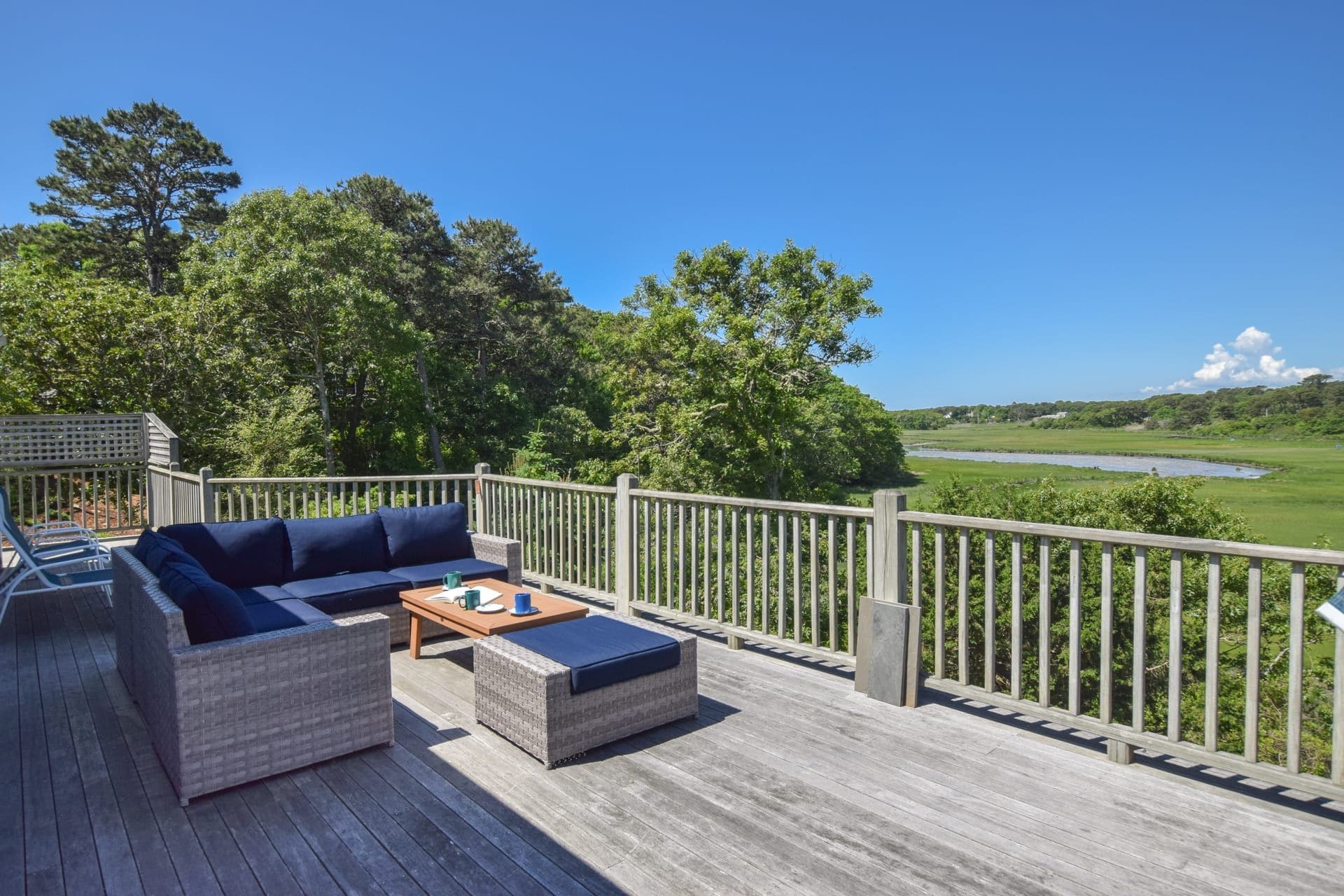 Une terrasse dotée de mobilier d’extérieur, offrant une vue sur une rivière et un paysage boisé.