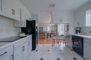 Cocina moderna con armarios blancos, un refrigerador negro y una zona de comedor con mesa y sillas.