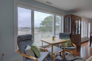 A room with a large window, a wooden cabinet, and two chairs with cushions.