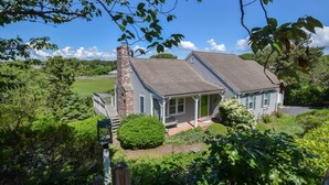 A two-story house with a brick chimney, a covered porch, and a well-maintained garden. - Stunning Marsh Views, Near Pleasant Street Beach! (Chatham)