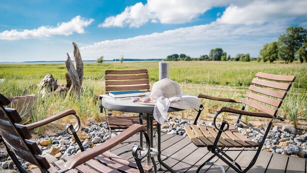 Une terrasse en bois avec deux chaises et une table, le tout installé devant un champ verdoyant et un ciel dégagé.