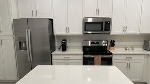 Uma cozinha moderna com armários brancos, uma geladeira de aço inoxidável, uma cafeteira, um micro-ondas e um forno.