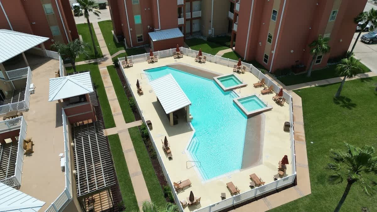Un área de piscina en la azotea con varias piscinas, sillas de descanso y palmeras.