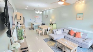 A modern living room with a grey sofa, a coffee table, and a dining area with a table and chairs. - Like New Killer Patio - Stunner Close to Beach (South Padre Island)
