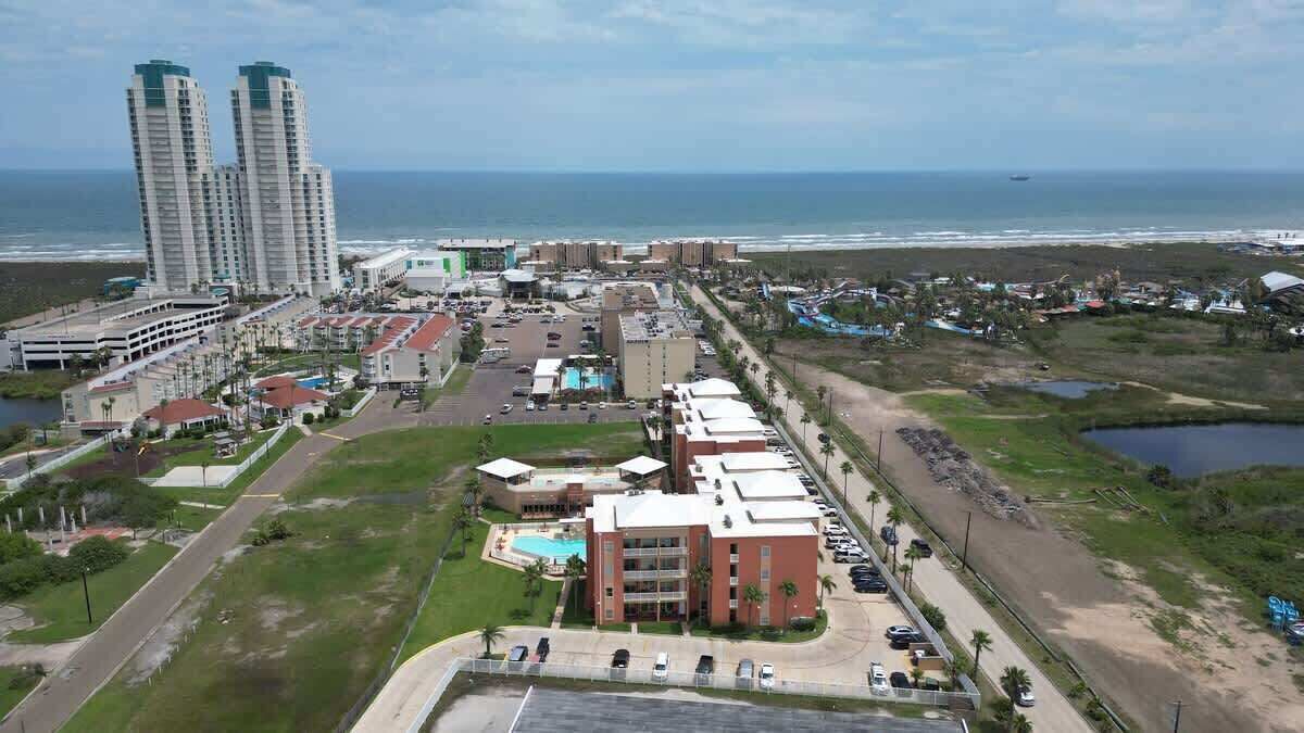 A coastal hotel with multiple buildings, a parking lot, and a view of the ocean.