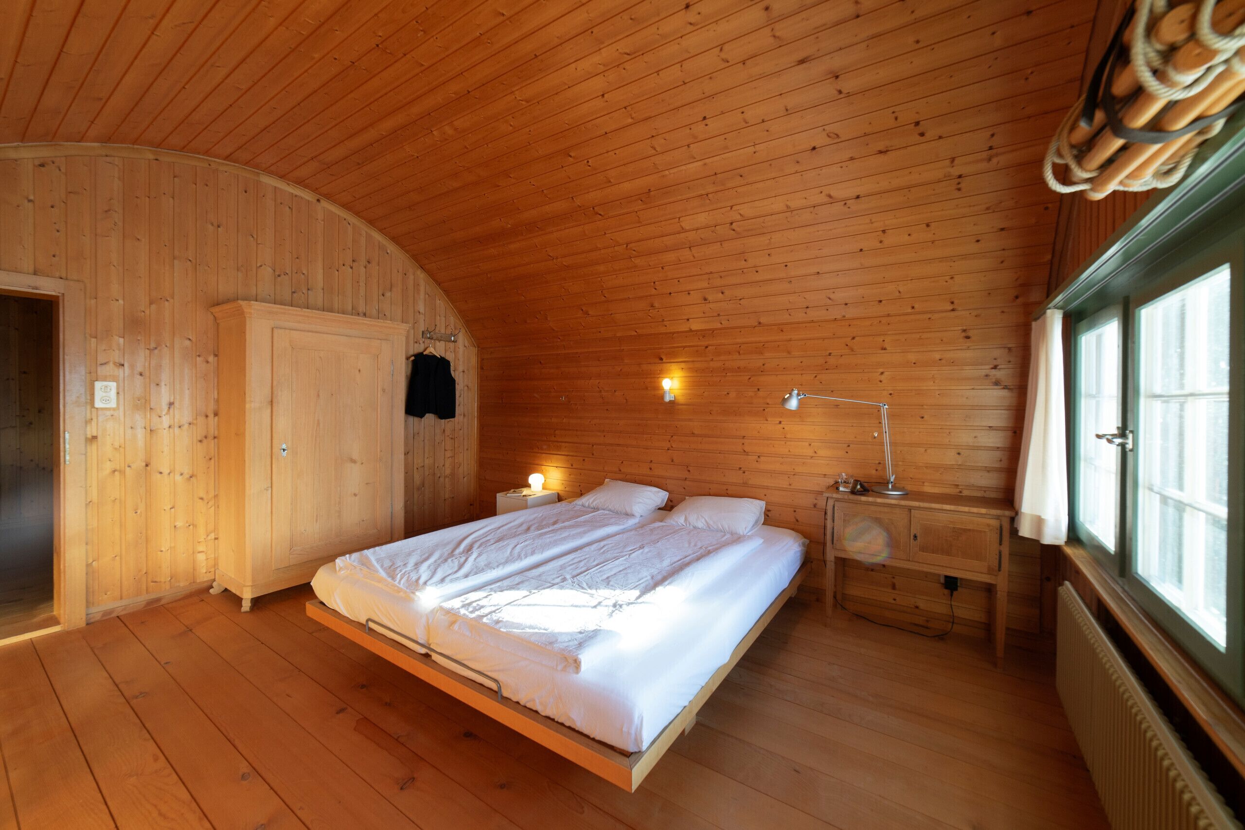 Un dormitorio con paneles de madera, una cama, lámparas de noche y una ventana.