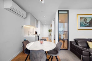 A modern kitchen with white cabinets, a built-in oven, and a dining area with a marble table and grey chairs.
