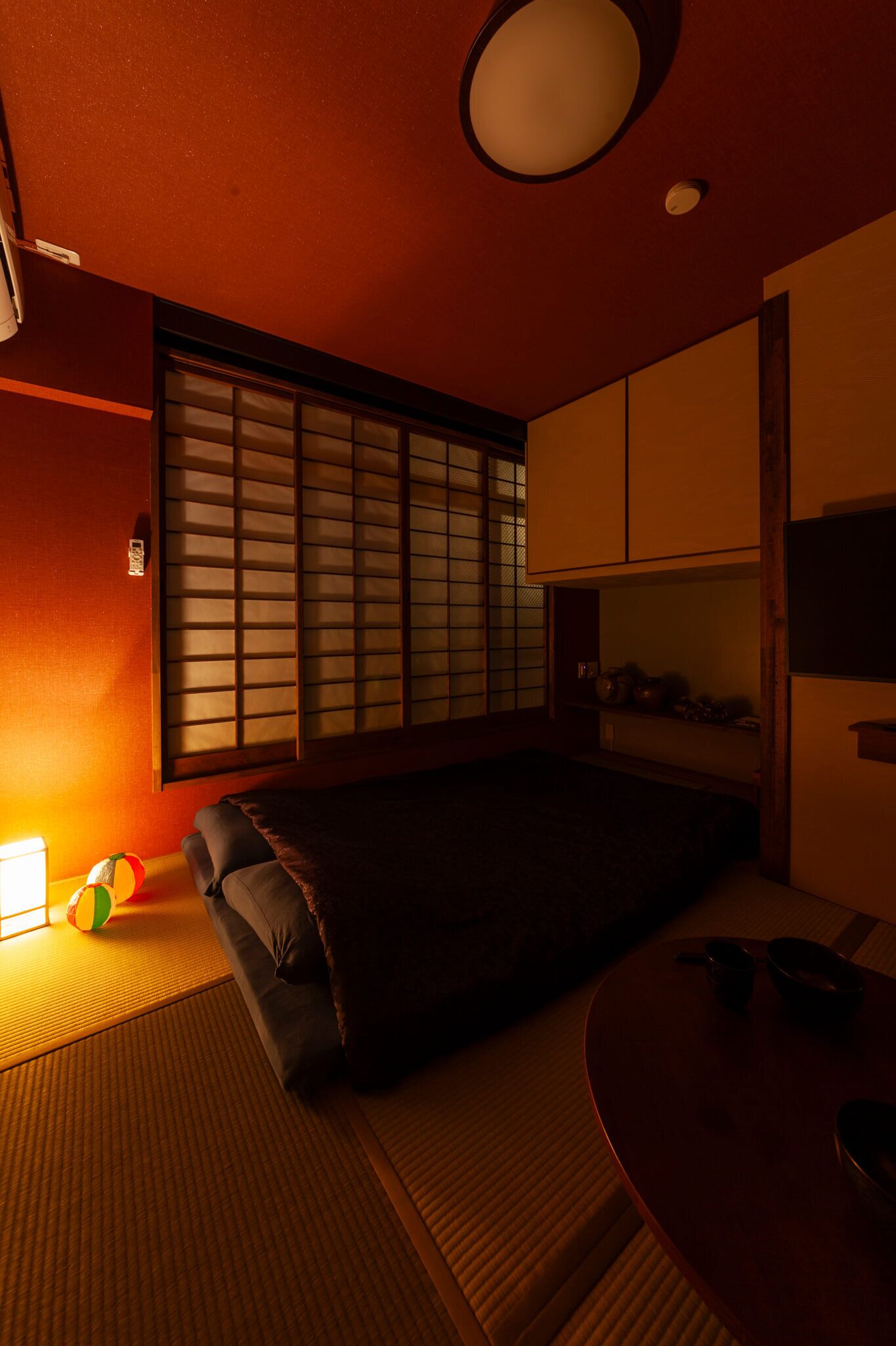 A room with tatami flooring, a futon bed, a shoji screen, and a traditional Japanese-style table with a bowl.