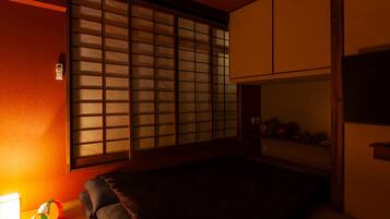 A room with tatami flooring, a futon bed, a shoji screen, and a traditional Japanese-style table with a bowl.