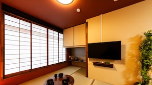 A traditional Japanese room with tatami flooring, a low table with black bowls, a TV mounted on the wall, and a sliding door with a grid pattern. - Oyadokinokuniya Isemachi (Nagasaki)