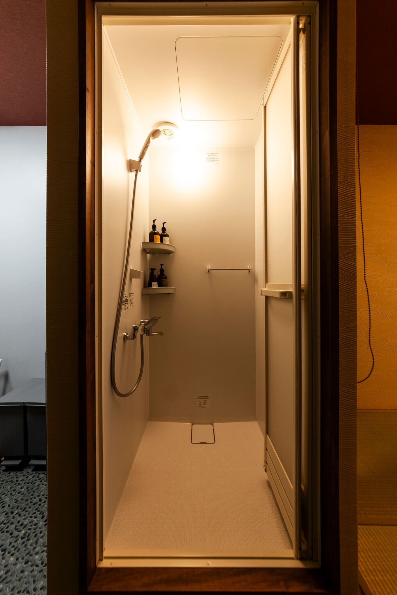 A small, enclosed shower area with a handheld showerhead, a shelf with toiletries, and a towel rack.