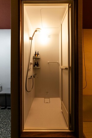 Un petit espace douche fermé, équipé d’un pommeau de douche à main, d’une étagère pour les articles de toilette et d’un porte-serviettes.