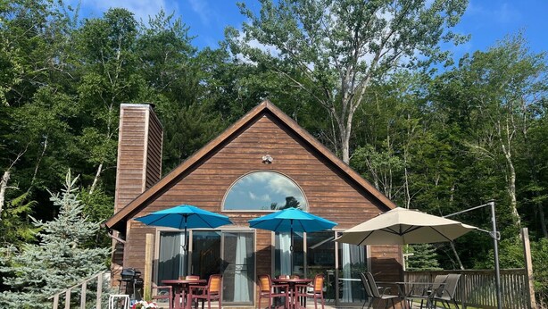 A wooden cabin with a deck, two blue umbrellas, and a red bench. - Waterfront close to Traverse City, Kayaks, Row Boat, Firepit, Dog ok, 8pl (Traverse City)