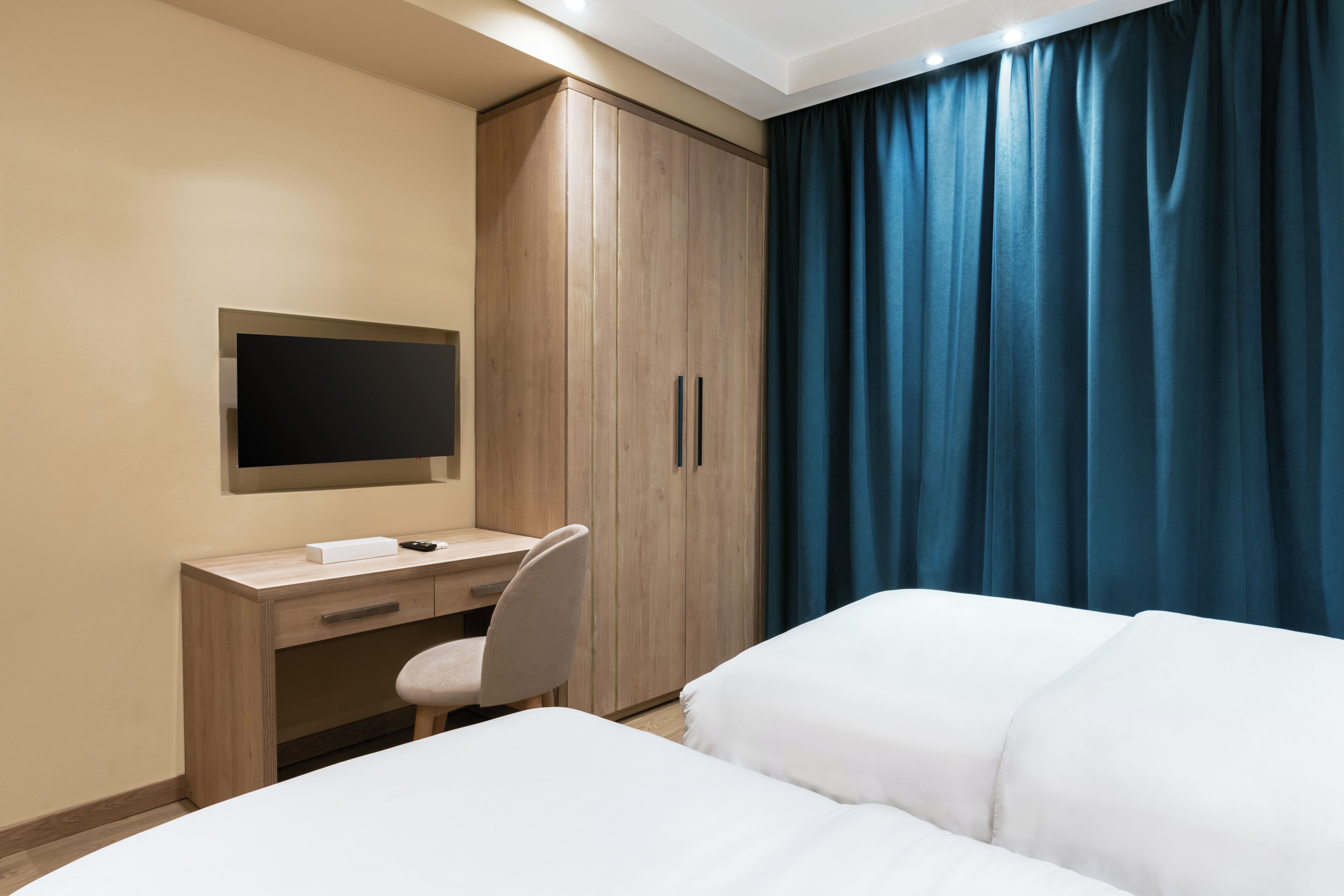 Ein Hotelzimmer mit einem Bett, einem Schreibtisch mit Stuhl, einem Kleiderschrank und einem an der Wand montierten Fernseher.
