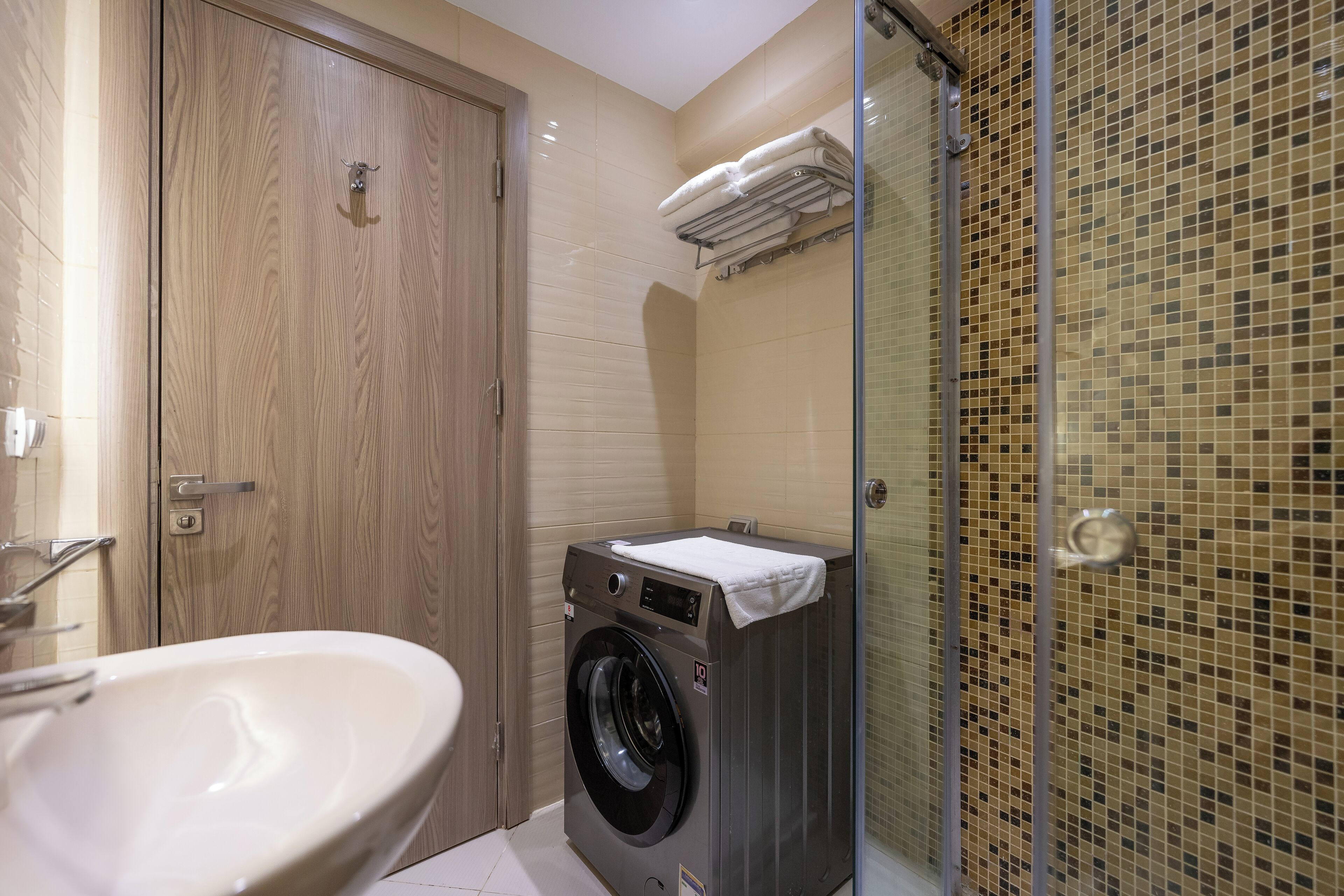 Un baño pequeño con lavadora, lavamanos y cabina de ducha de vidrio.