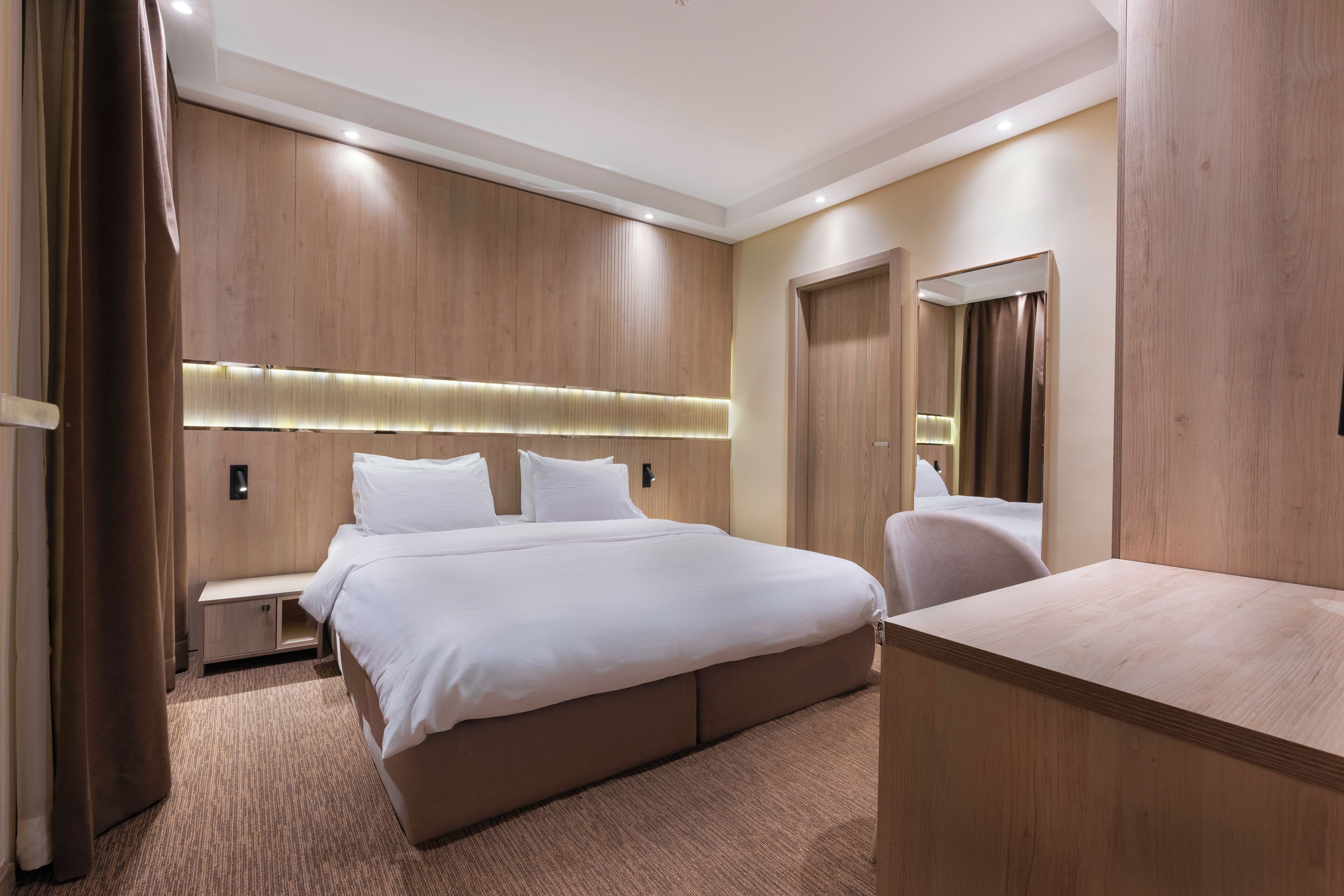 Quarto de hotel moderno com uma cama grande, mesa de cabeceira, guarda-roupa e espelho.