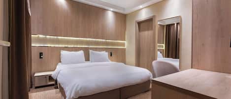 A modern hotel room with a large bed, a bedside table, a wardrobe, and a mirror.
