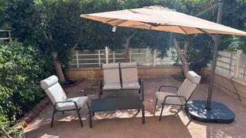 Un patio exterior con una mesa redonda, cuatro sillas y un paraguas grande.
