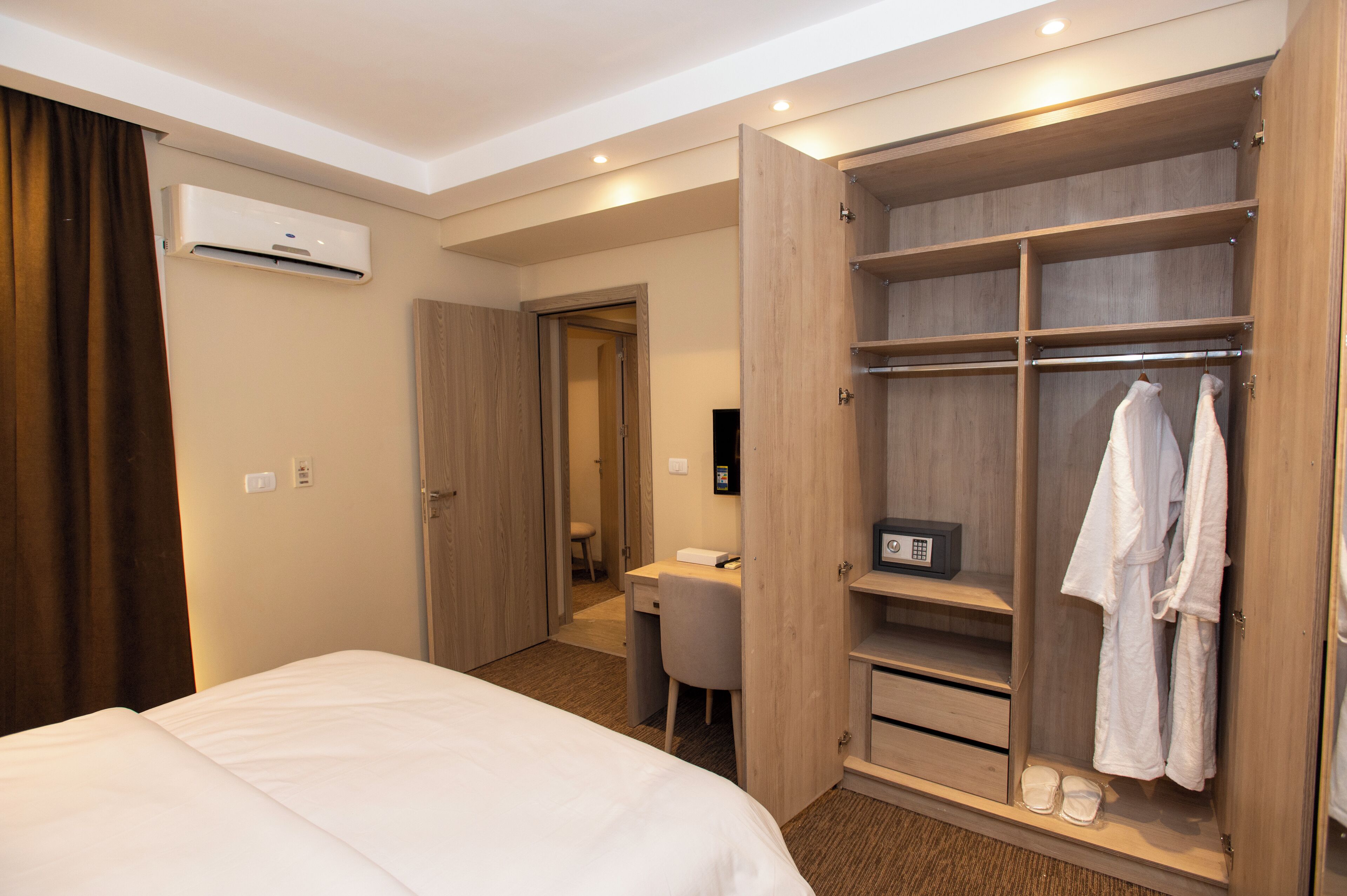 A hotel room with a bed, a desk, a walk-in closet, and an air conditioning unit.