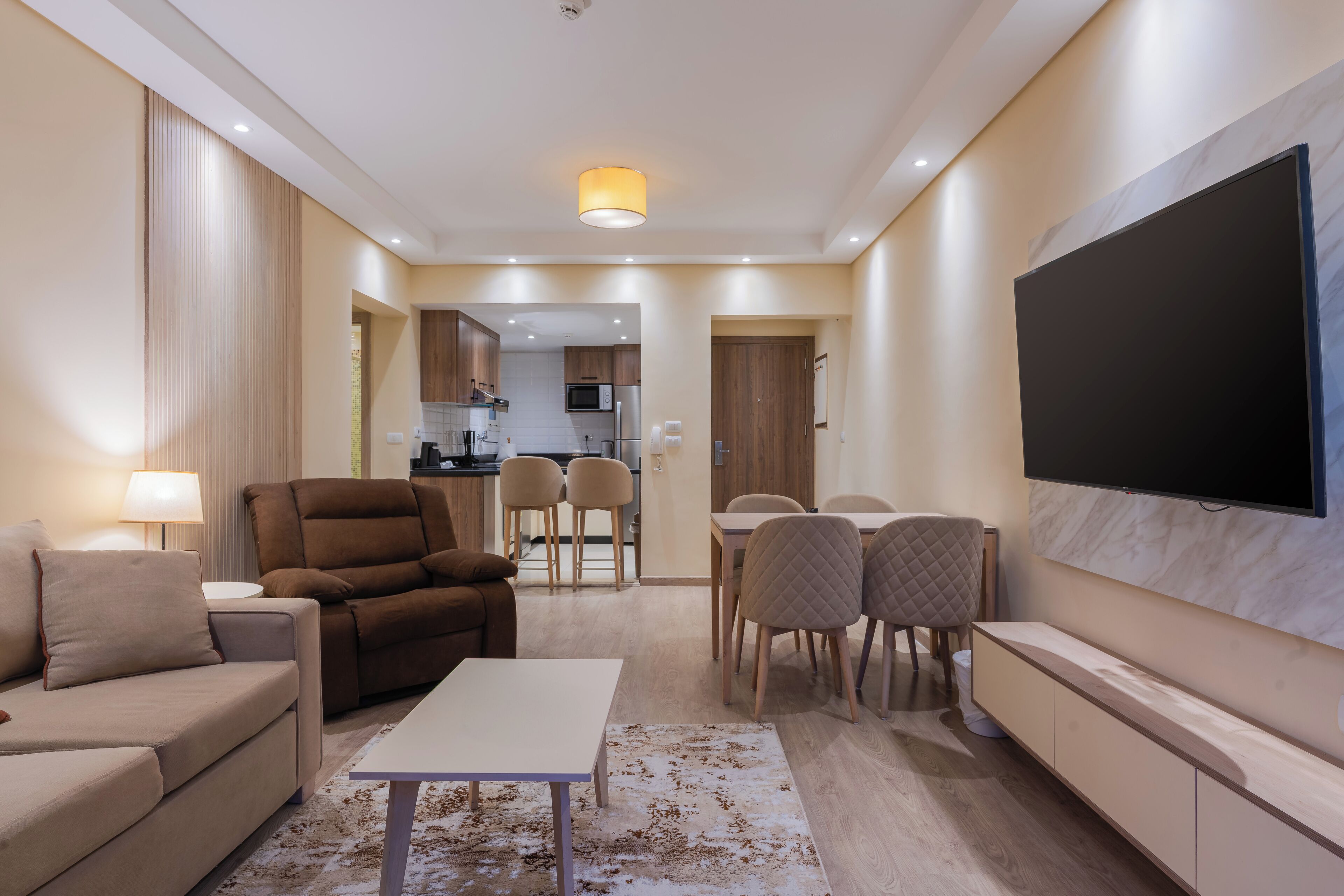 Una sala moderna con sofá, sillón, mesa de comedor y sillas. Un televisor de pantalla plana está montado en la pared.