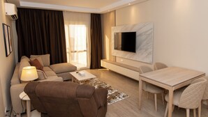 Una sala de estar moderna con un sofá, una mesa de centro, un televisor montado en la pared y una zona de comedor con mesa y sillas.