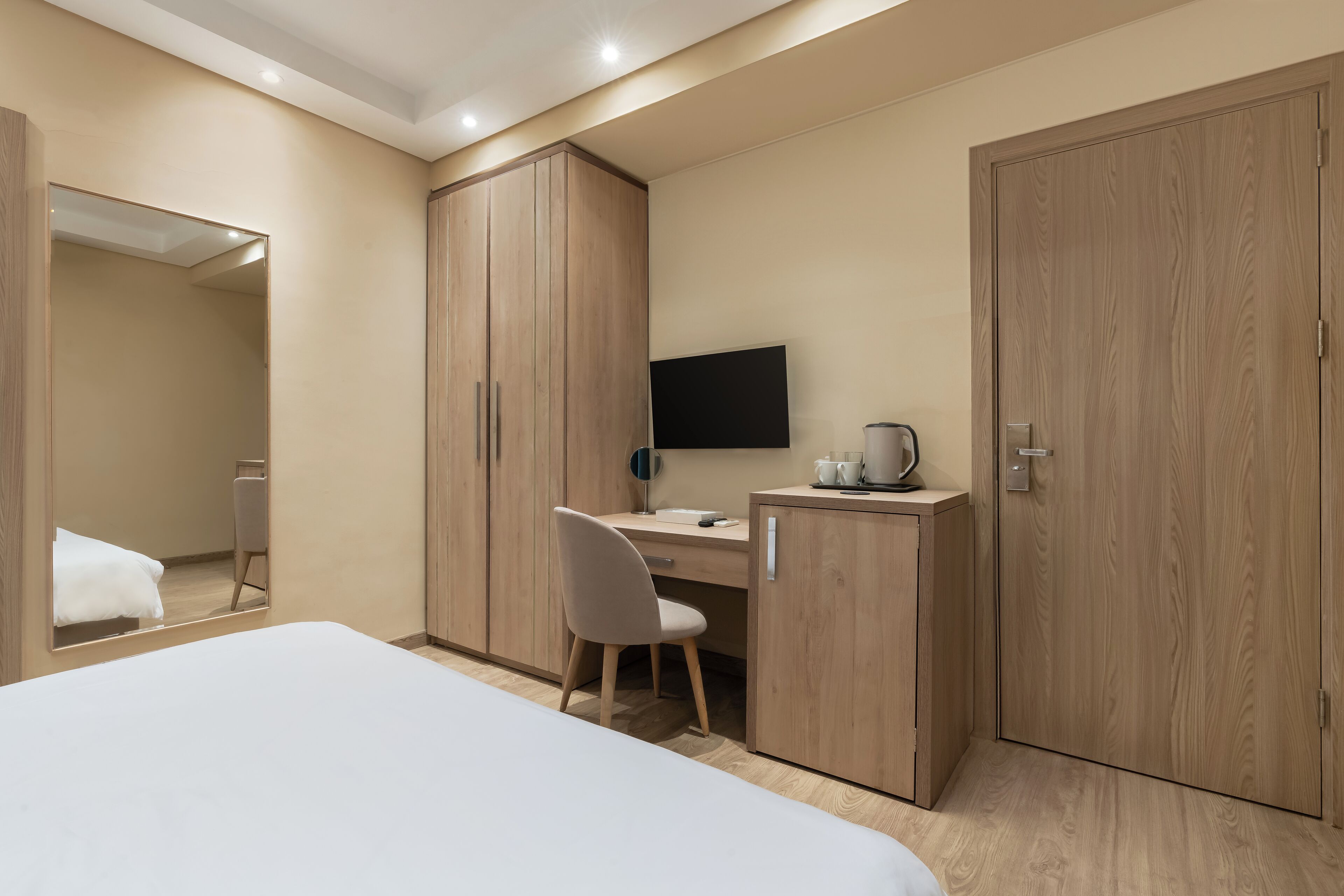 A hotel room with a bed, a desk, a chair, a TV, and wooden wardrobes.