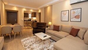 Una sala moderna con sofá, sillón, mesa de comedor y sillas. Hay un control remoto sobre una mesa auxiliar.