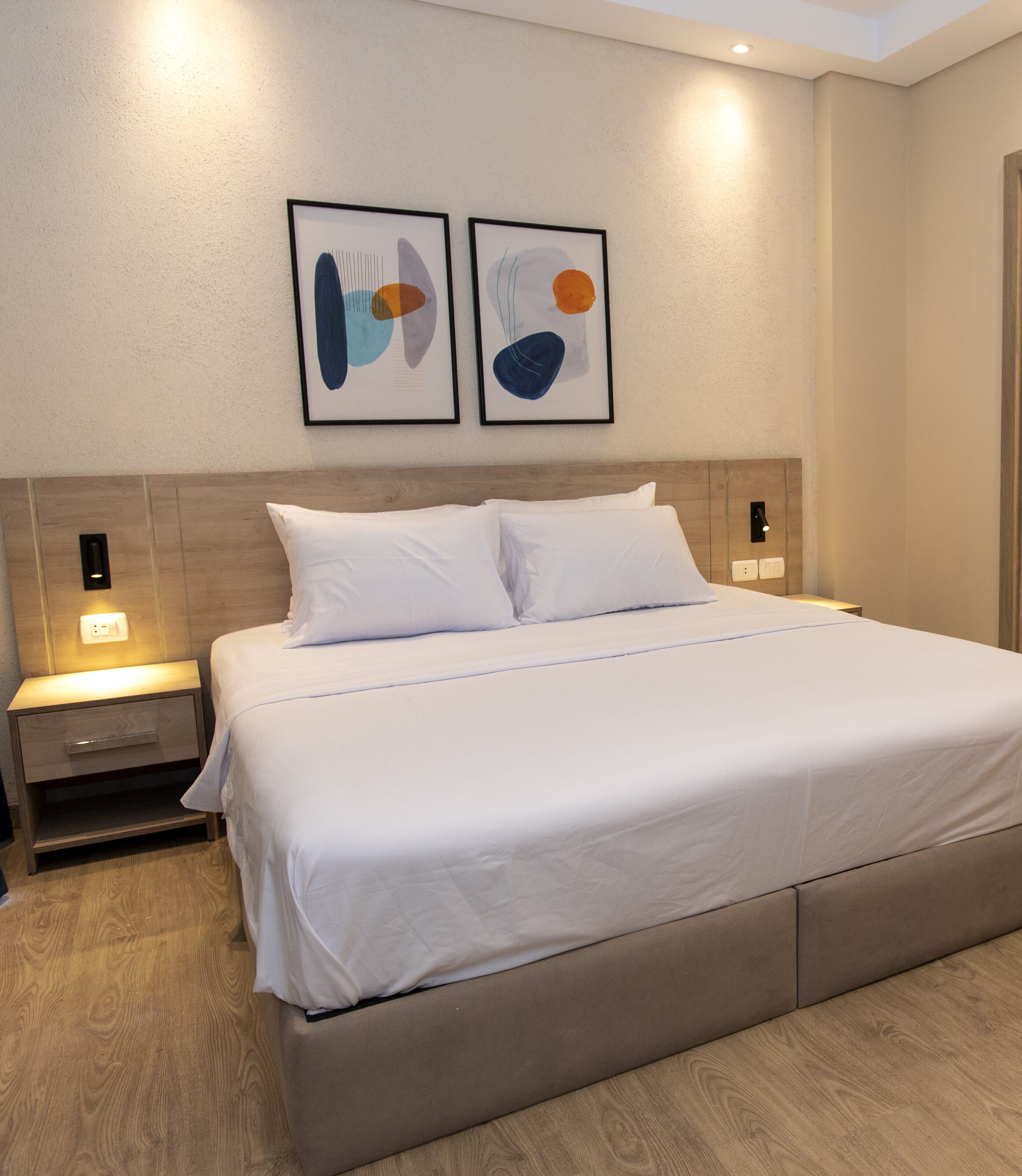 A modern hotel room with a large bed, two bedside tables, and abstract artwork on the wall.
