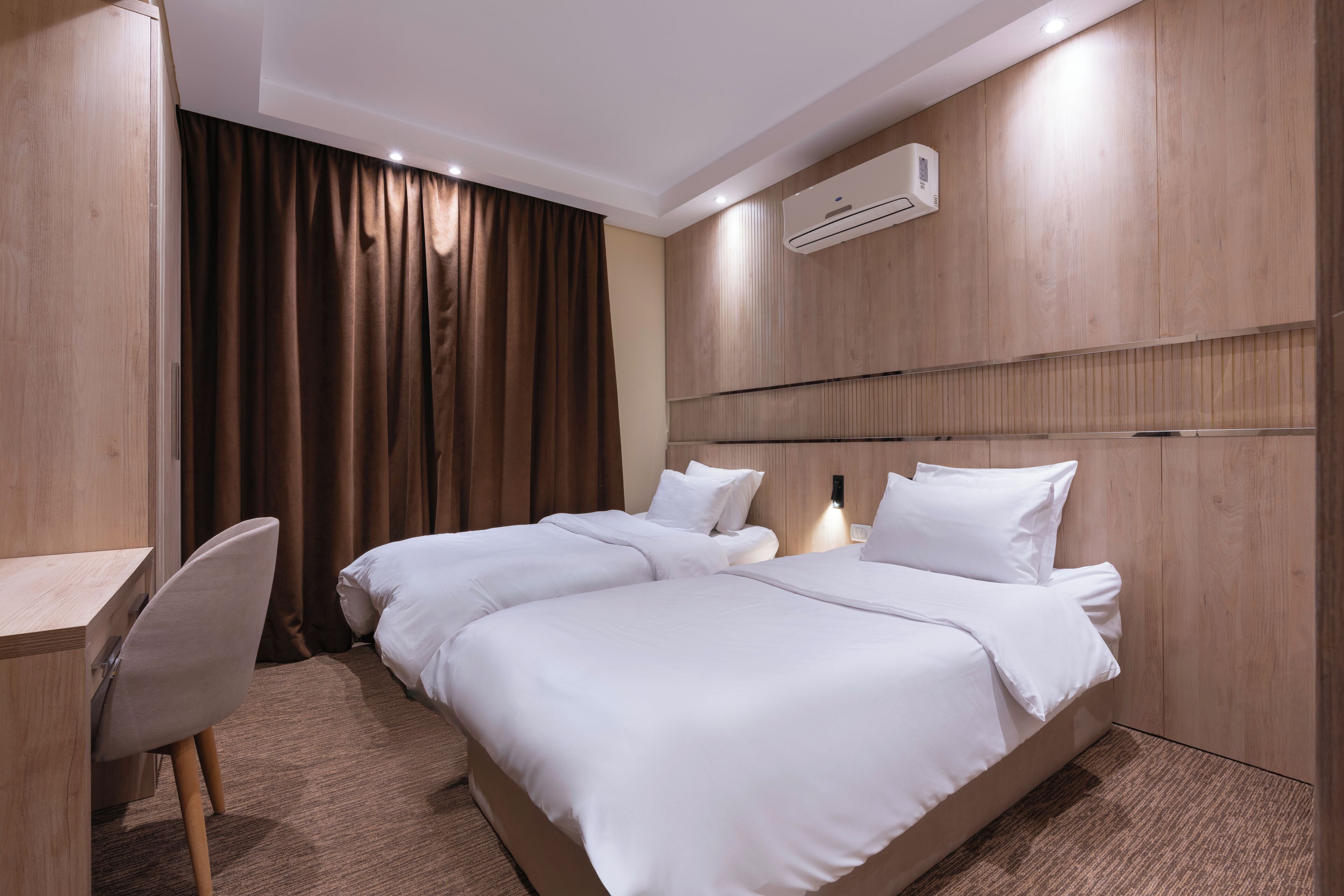 A hotel room with two beds, a desk, and an air conditioning unit.
