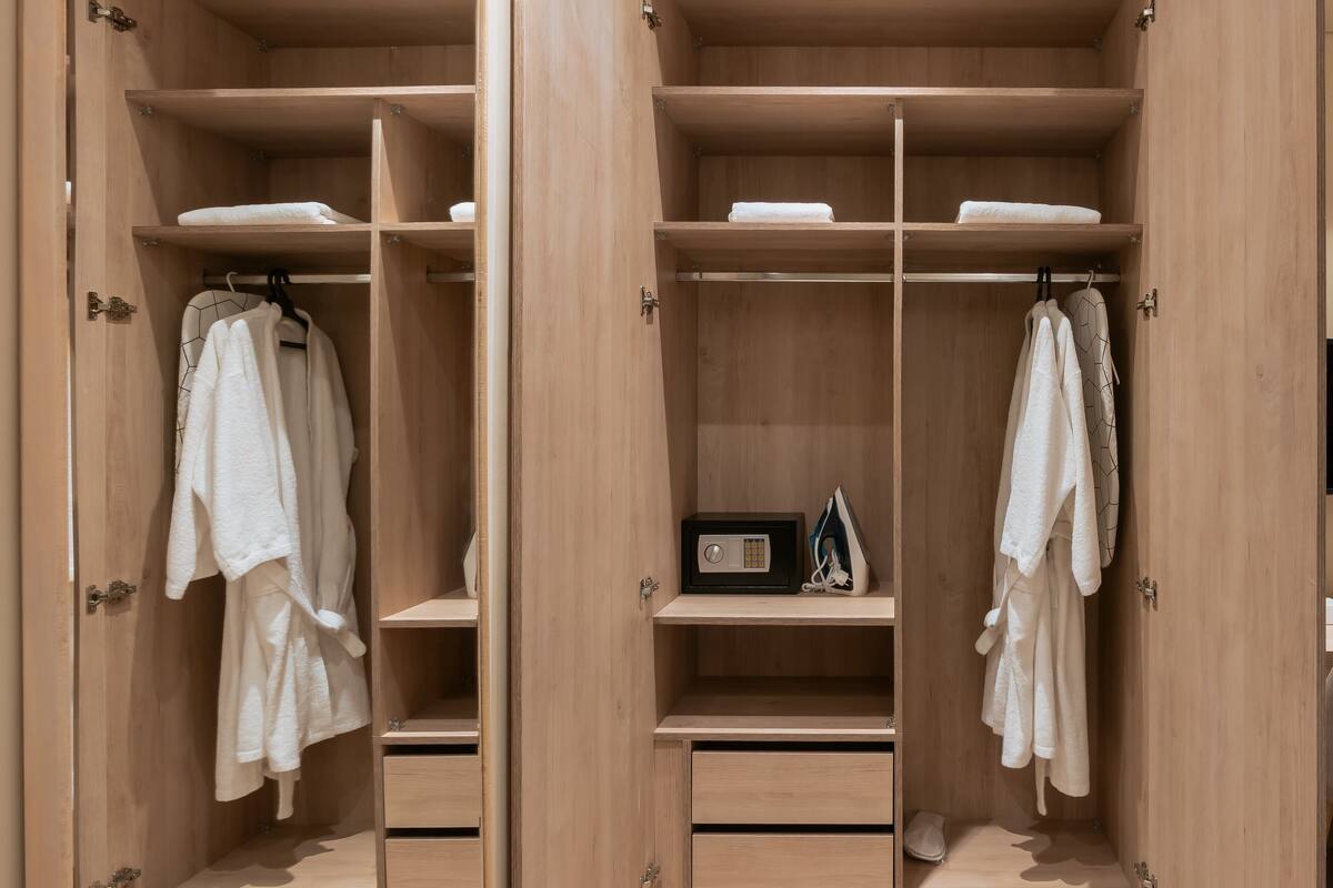 A wooden walk-in closet with multiple shelves, hanging space, and drawers.