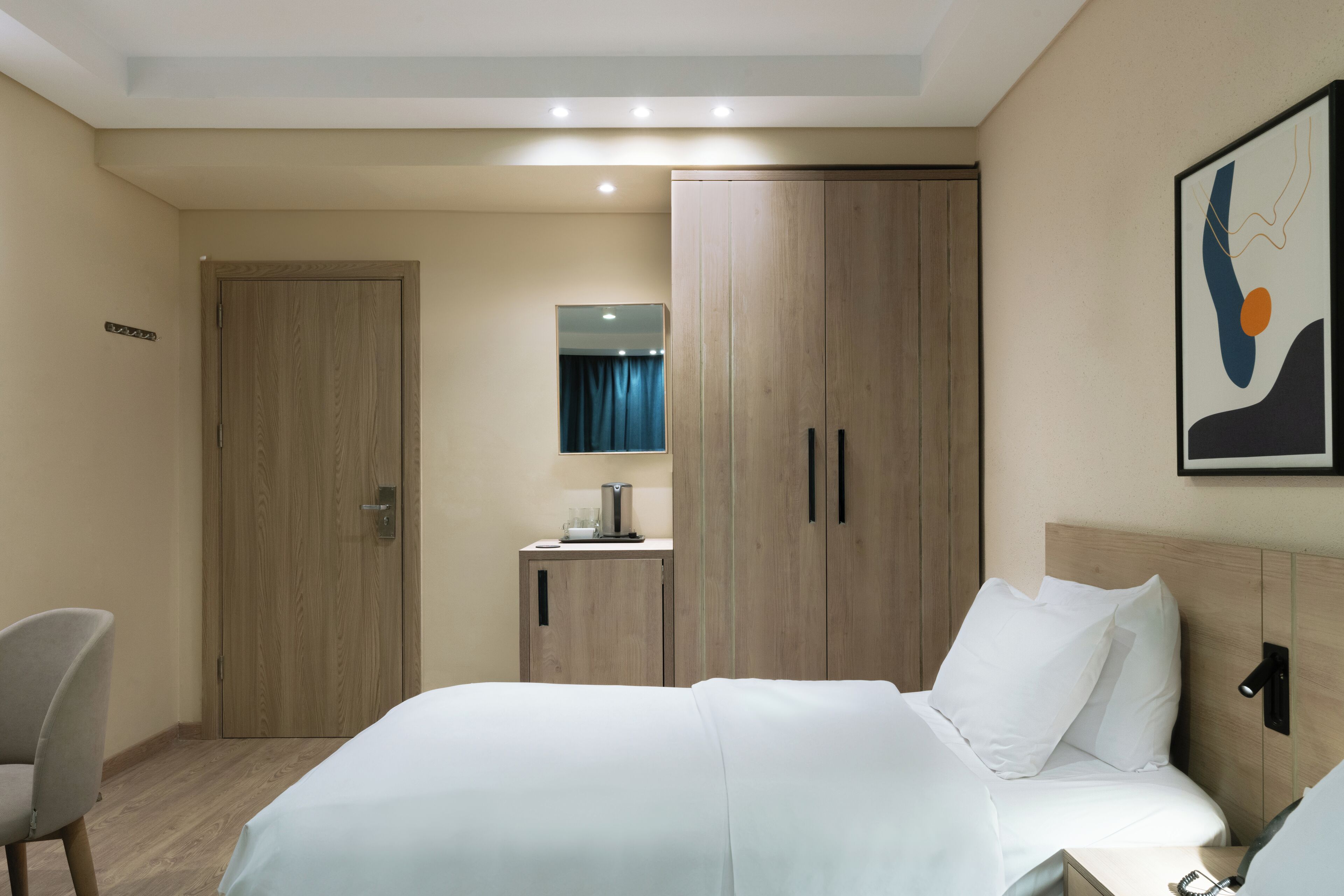 A hotel room with a bed, a desk, a wardrobe, and a mirror.