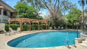 Une piscine dotée d’une terrasse en bois et de chaises longues, entourée d’arbres et abritée par une zone couverte.