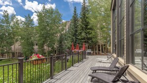 A wooden deck with outdoor furniture and a view of a garden and trees.
