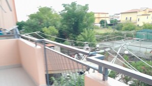 A balcony with a metal railing, a tiled floor, and a view of greenery and buildings in the background. - Intero appartamento 70mq  (Scalea)