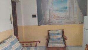 A room with a sofa and a chair, a mural of a beach scene, and a door. - Intero appartamento 70mq  (Scalea)